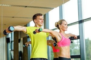 smiling man and woman with dumbbells in gym